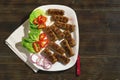 Balkan cuisine. Cevapi - grilled dish of minced meat - with vegetables. Dark rustic background, flat lay, free space for text Royalty Free Stock Photo