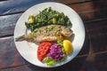 Balkan cuisine. Grilled fish with vegetables on white plate. Dark rustic background, flat lay