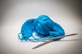 A ball of blue yarn on a white background with knitting needles