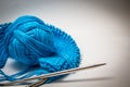 A ball of blue yarn on a white background with knitting needles