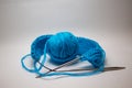 A ball of blue yarn on a white background with knitting needles