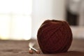 A ball of brown woolen threads and two wooden knitting needles close-up.