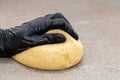 A ball of dough is kneaded by a man in black gloves. Baker& x27;s hands knead dough with gloves on a gray table Royalty Free Stock Photo