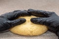 A ball of dough is kneaded by a man in black gloves. Baker& x27;s hands knead dough with gloves on a gray table. Royalty Free Stock Photo