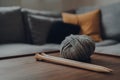 Ball of grey chunky wool yarn and a pair of large wooden knitting needles on a table