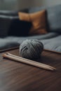 Ball of grey chunky wool yarn and a pair of large wooden knitting needles on a table