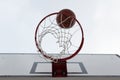 Ball inside red basketball hoop, basket against white sky. Outdoor basketball court. White board. Royalty Free Stock Photo