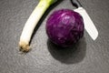 ball of red cabbage, a leek and a kitchen knife on a black granite table. Red cabbage ready to be cooked together with leek in Royalty Free Stock Photo
