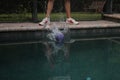 Ball splashing into the pool water on the background of the legs of a person standing at poolside