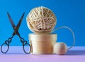 Ball of string on a wooden pedestal with a pair of ornate scissors on a blue and pink background , concept of hobbys and pastimes