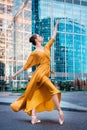Ballerina, ballet dancer in yellow gown dancing on blue street city background. Graceful