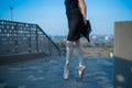 Ballerina in ballet legs in shoes and black tutu dancing by the fence. Beautiful young woman in black dress and pointe dancing