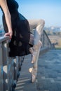 Ballerina in ballet legs in shoes and black tutu dancing by the fence. Beautiful young woman in black dress and pointe