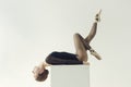 ballerina in a black bodysuit lies on a cube with her head thrown back and one leg stretched up