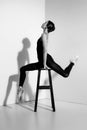 Ballerina in black outfit posing on a wooden chair, studio background. Royalty Free Stock Photo