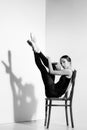 Ballerina in black outfit posing on a wooden chair, studio background. Royalty Free Stock Photo