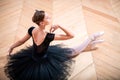 Ballerina in a black tutu sitting on floor with her back to the camera