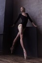ballerina in a bodysuit and pointe shoes is standing in the corner of the room looking out the window Royalty Free Stock Photo
