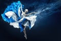 Ballerina dancing in Blue Chiffon Dress over Night Sky Background. Ballet Dancer jumping in fluttering Skirt pointing towards Hand