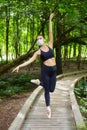 A ballerina in a mask and pointe shoes is doing exercises on a wooden path in a forest park. safe outdoor training concept