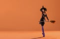 A ballerina on pointe shoes in a black witch costume in a hat and with a broom dances on an orange background