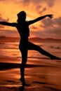 A ballerina with a silhouette shape performs ballet movements very flexibly on the beach with the waves crashing