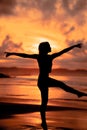 A ballerina with a silhouette shape performs ballet movements very flexibly on the beach with the waves crashing