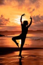 A ballerina with a silhouette shape performs ballet movements very flexibly on the beach with the waves crashing