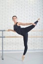 Ballerina stretches herself near barre at ballet studio, full length portrait, performing twine. Royalty Free Stock Photo