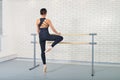 Ballerina stretches herself near barre at ballet studio, full length portrait, shoot from behind. Royalty Free Stock Photo
