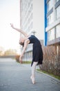 Ballerina in a tutu posing in front of a multi-storey residential building. Beautiful woman in black dress and pointe