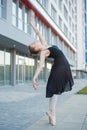 Ballerina in a tutu posing in front of a multi-storey residential building. Beautiful young woman in black dress and pointe shoes