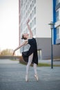 Ballerina in a tutu posing in front of a multi-storey residential building. Beautiful young woman in black dress and