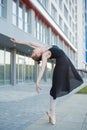 Ballerina in a tutu posing in front of a multi-storey residential building. Beautiful young woman in black dress and