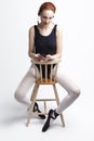 Ballet Concepts. Portrait of Female Ballet Dancer in Body Suit Sitting On Chair and Listening Music on Headphones. Against White