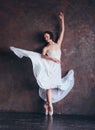 Ballet dancer ballerina in beautiful thin flying white dress is posing in dark loft studio