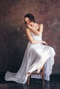 Ballet dancer ballerina in beautiful thin flying white dress is posing in dark loft studio