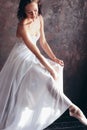 Ballet dancer ballerina in beautiful thin flying white dress is posing in dark loft studio