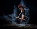 Ballet dancer in black bodysuit jumps high and dance with flour on the beach in the evening. Women`s street ballet. Flour, talc, Royalty Free Stock Photo