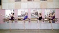 In dancing hall, Young ballerinas in purple leotards perform attitude efface on pointe shoes, standing near barre at