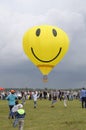 Balloon with the smiley face symbol on it flying above the field with crowd of people walking around