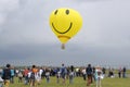 Balloon with the smiley face symbol on it flying above the field with crowd of people walking around