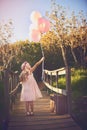 Balloons make me happy. a happy little girl holding balloons and a teddy bear while standing in the middle of a bridge. Royalty Free Stock Photo