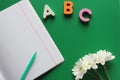 Ballpoint pen and a blank school notebook next to the letters ABC and white chrysanthemums on a green background