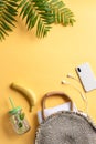 Bamboo bag, beach towel, palm leaves, phone with earphones, banana and ice drink in a glass mug over yellow background.