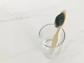 Charcoal infused bamboo toothbrush in glass with marble white background. Top view.