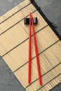 Bamboo mat with pair of red chopsticks and rest on grey, top view Royalty Free Stock Photo