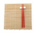 Bamboo mat with pair of red chopsticks and rest isolated on white, top view Royalty Free Stock Photo