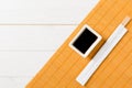 Bamboo mat and soy sauce with sushi chopsticks on white wooden table. Top view with copy space background for sushi. Flat lay Royalty Free Stock Photo