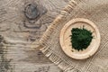 Bamboo plate with green chlorella powder on canvas linnen napkin on wooden background, top view, copy space